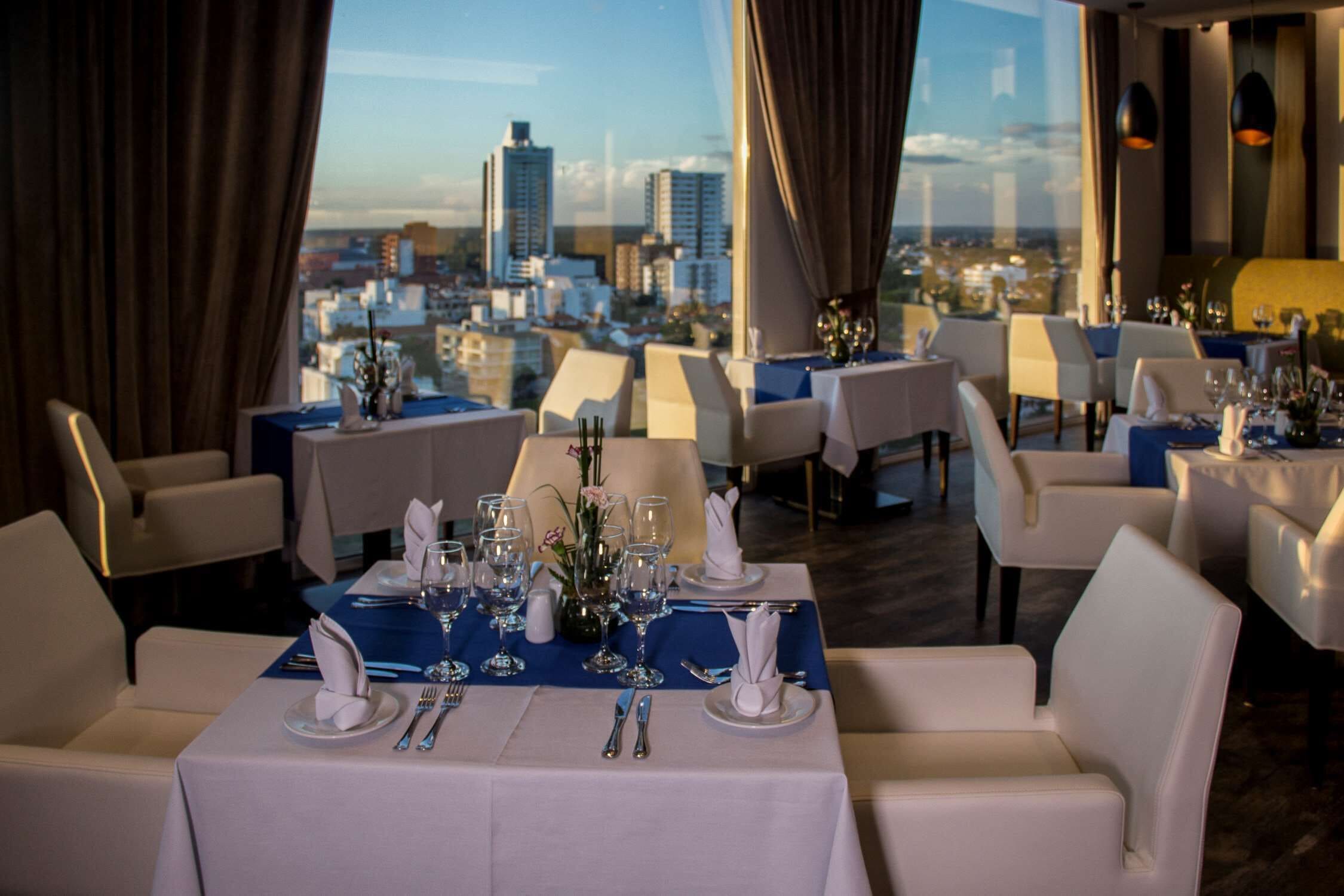 Un restaurante con mesas dispuestas para comer, que ofrece vistas de la ciudad a través de amplias ventanas.