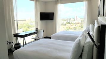 Quarto de hotel com duas camas, uma mesa, uma cadeira, televisão e vista para a cidade.