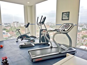 A gym with two treadmills and a stationary bike, large windows with a city view, and a small red fire extinguisher on the floor. - Hampton by Hilton Santa Cruz/Equipetrol, Bolivia (Santa Cruz)