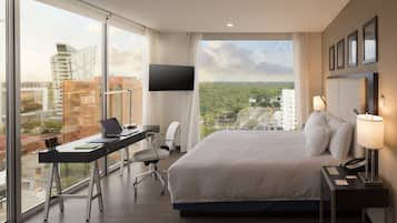 Habitación de hotel con una cama grande, un escritorio con una computadora portátil, una silla, un televisor y una mesita de noche con una lámpara.