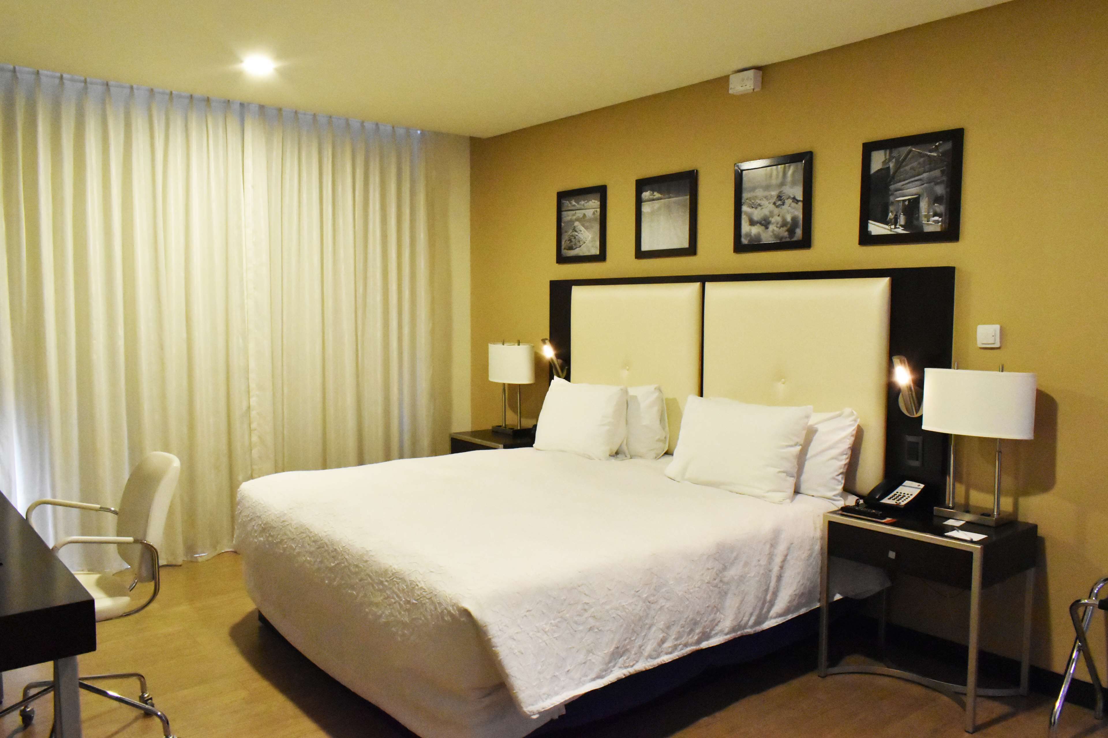 A hotel room with a large bed, two bedside tables with lamps, a desk, and a chair.