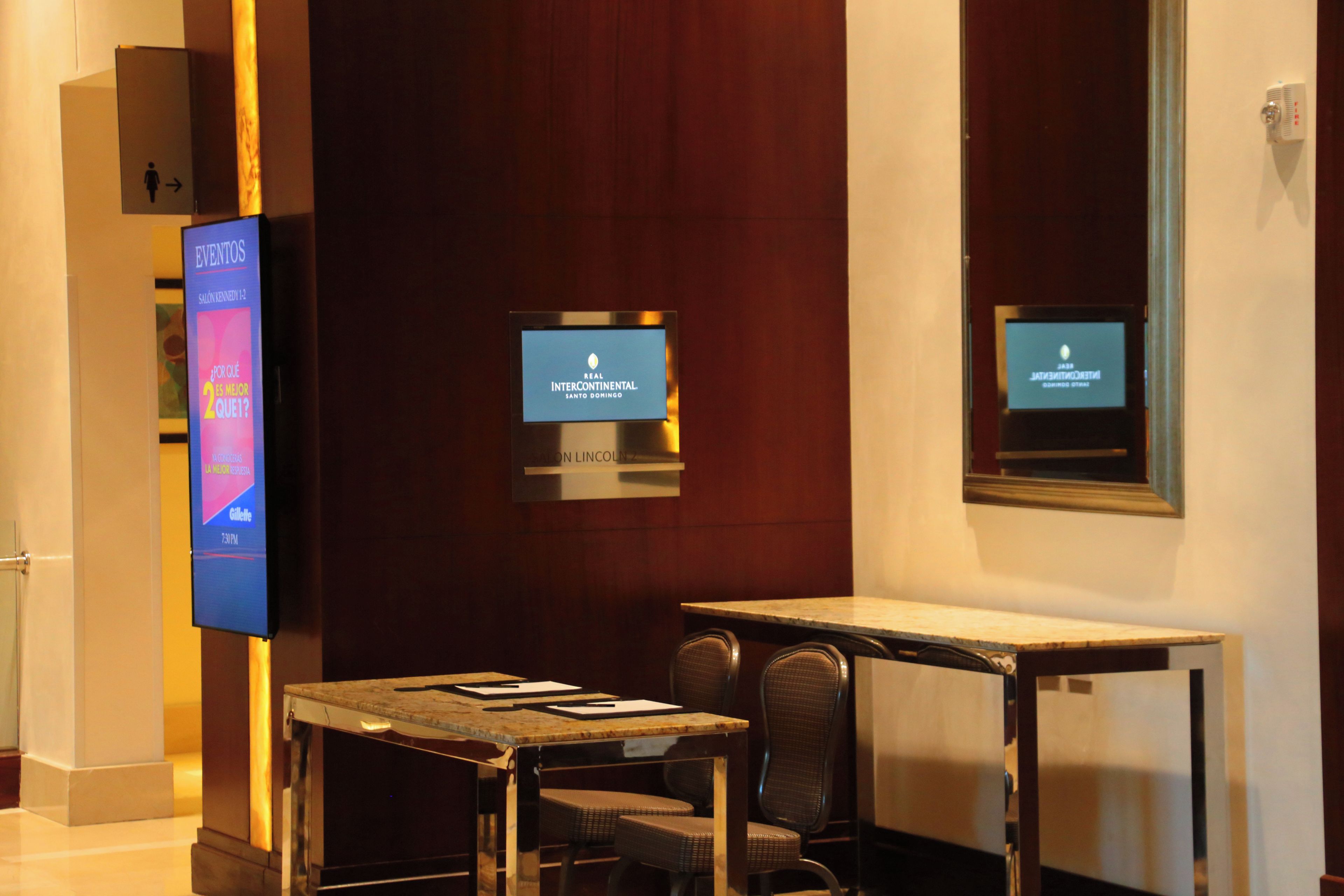 Een hotel lobby met een receptiebalie, een zithoek en digitale schermen met informatie.