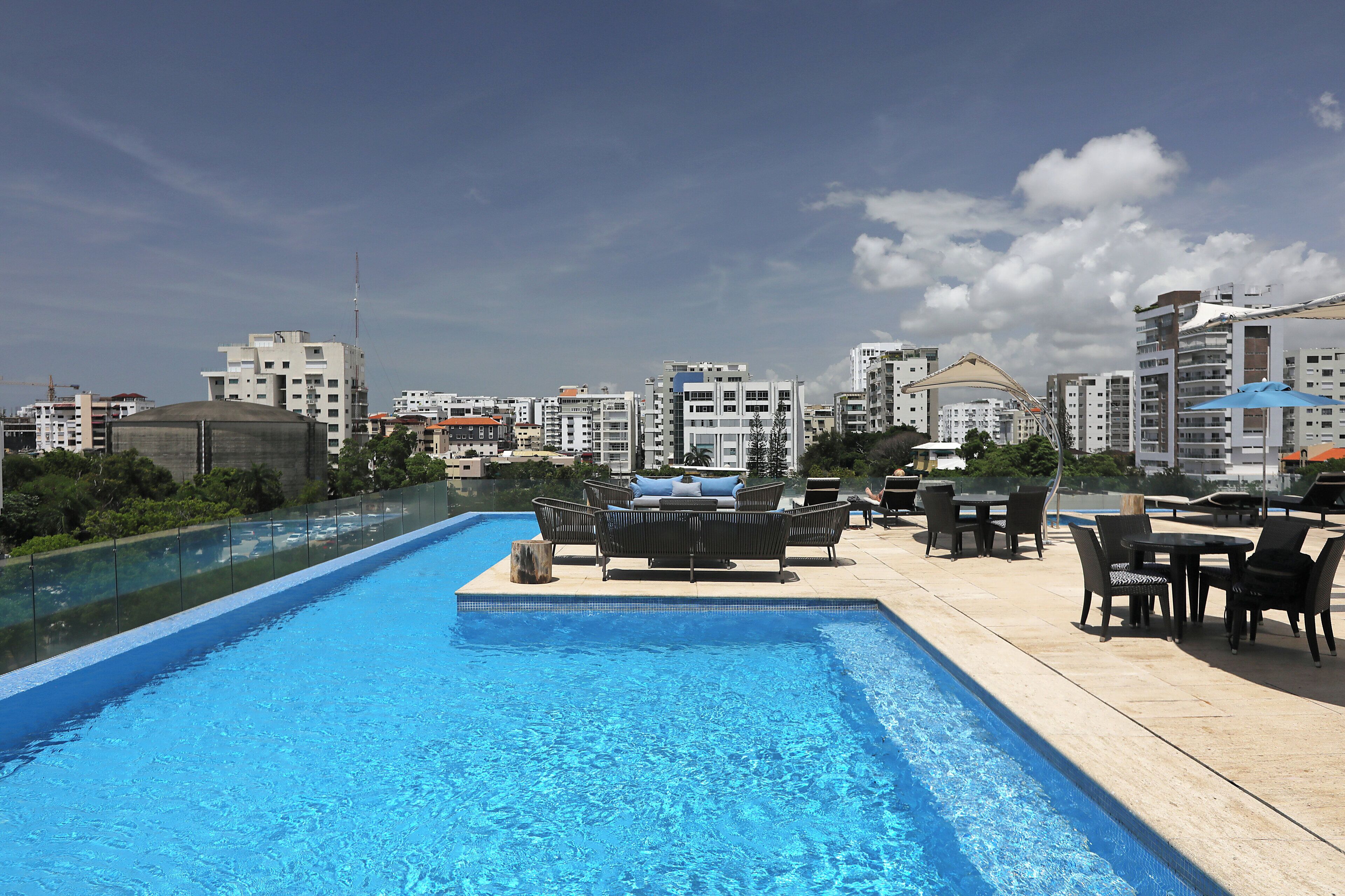A rooftop pool with lounge chairs and tables, surrounded by high-rise buildings.