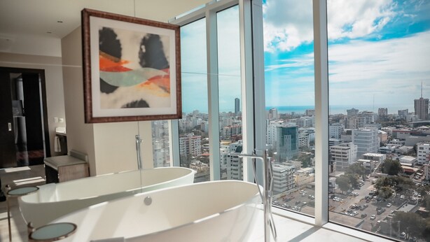 Een moderne badkamer met een ruim bad en een stadszicht door ramen van de vloer tot aan het plafond.