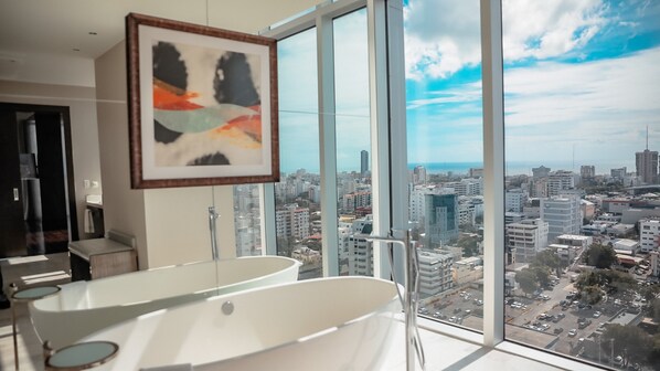 Een moderne badkamer met een ruim bad en een stadszicht door ramen van de vloer tot aan het plafond.