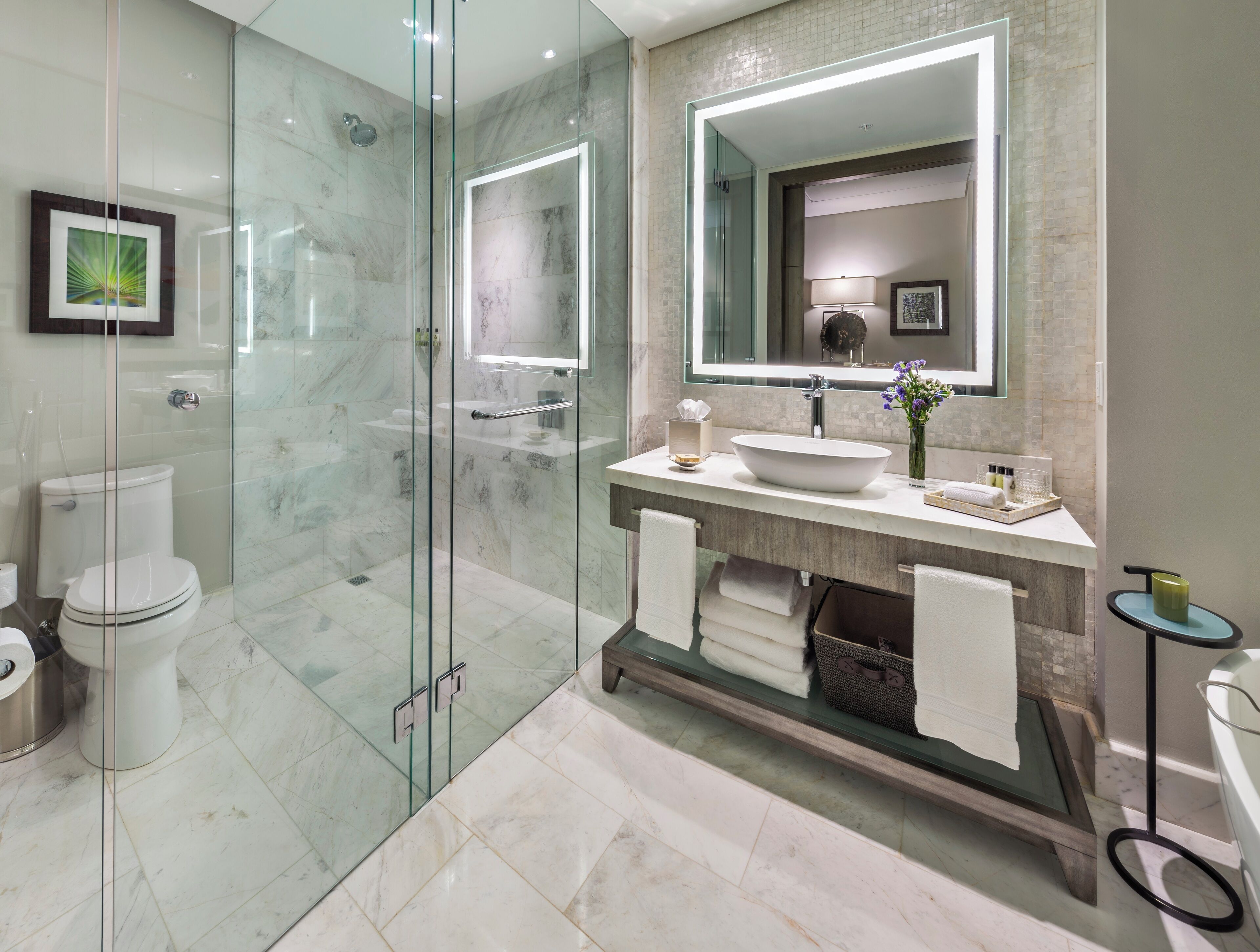 A modern bathroom with a glass-enclosed shower, a large mirror, and a marble-tiled floor.