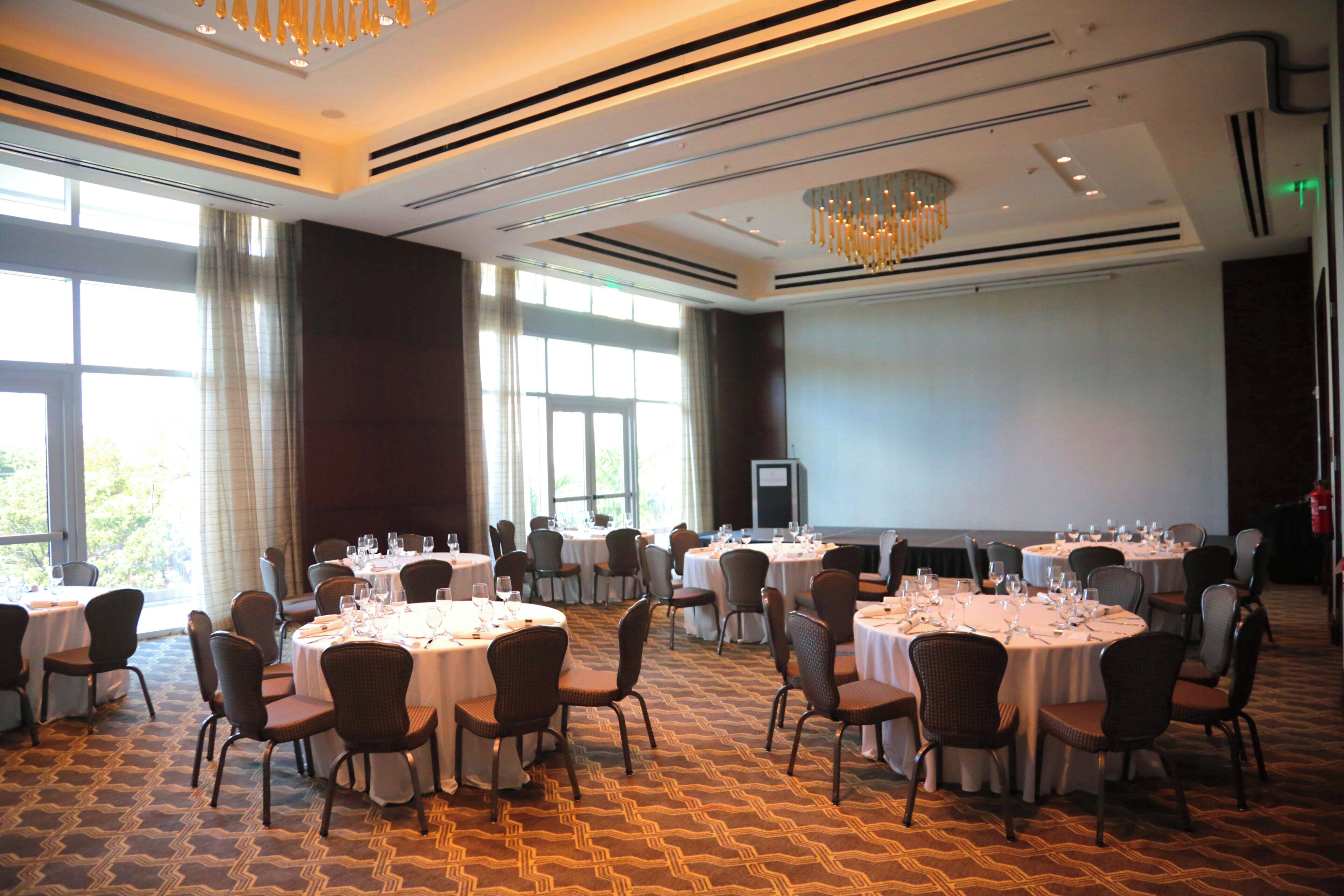 A conference room with multiple round tables, chairs, and a large screen.
