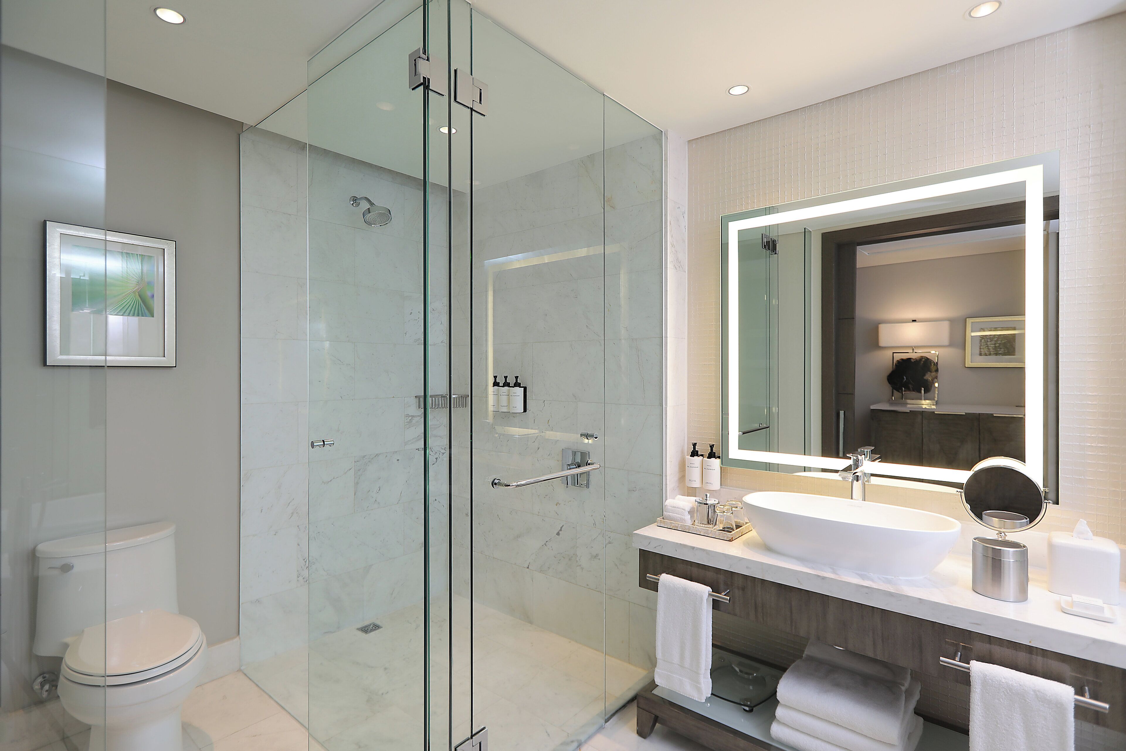 A modern bathroom with a glass-enclosed shower, a large sink, and a mirror with integrated lighting.