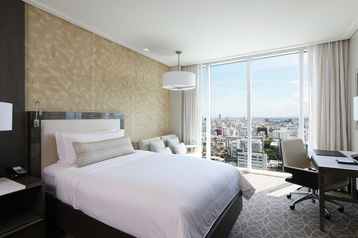 A hotel room with a large bed, a desk, and a view of the city.