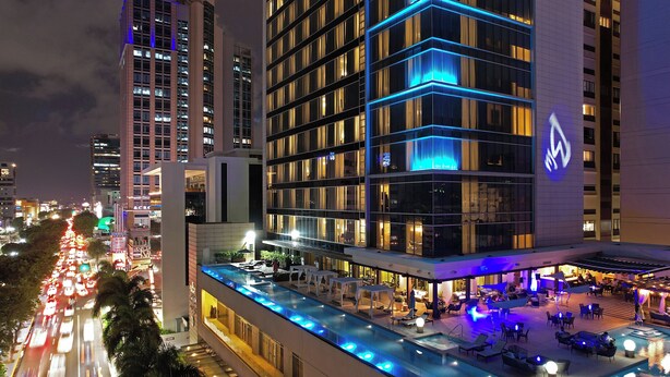 A hotel with a rooftop pool area, multiple floors, and a prominent logo on the building facade.