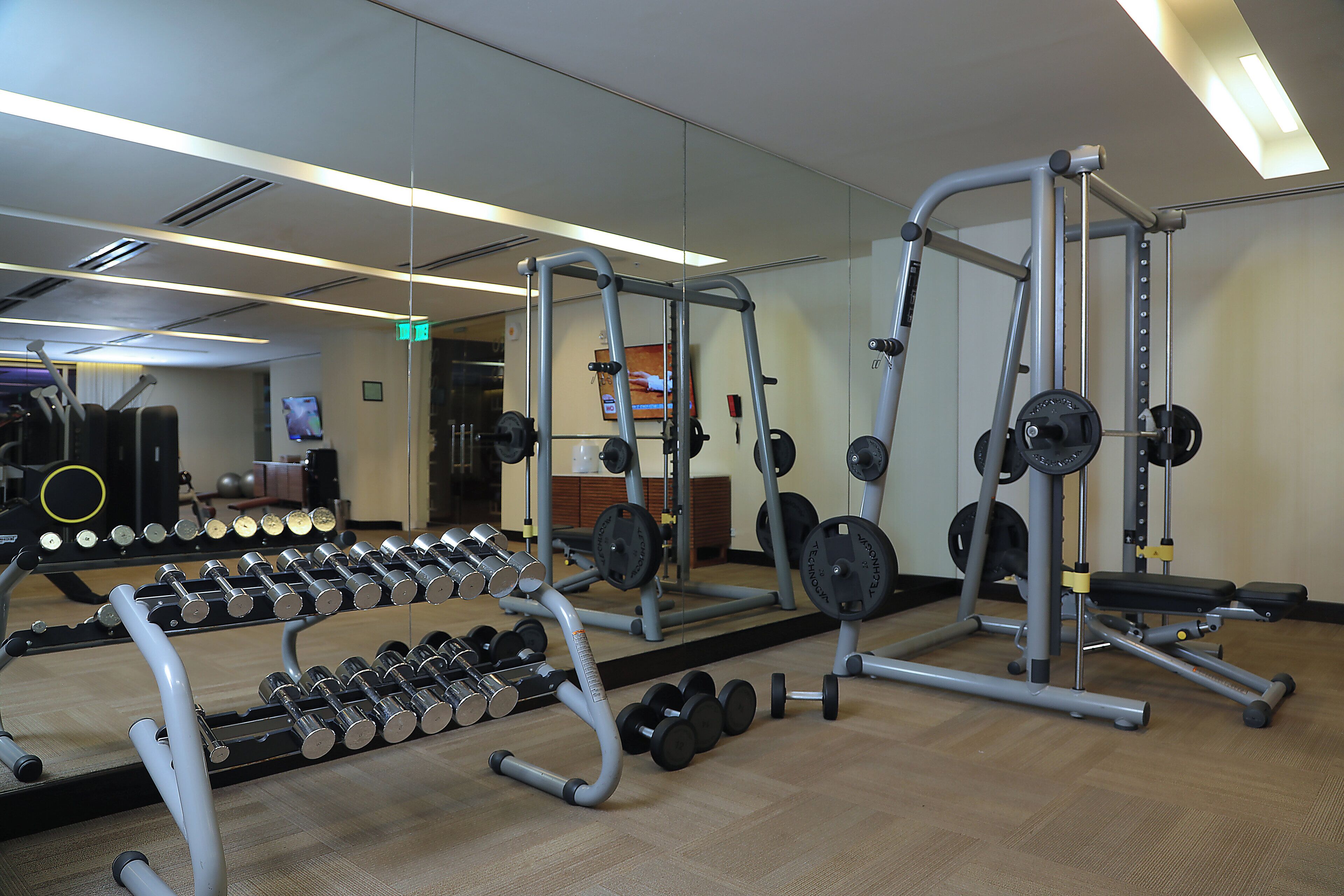 A gym with weightlifting equipment, mirrors, and a wooden floor.