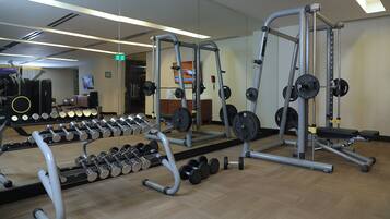 A gym with weightlifting equipment, mirrors, and a wooden floor.