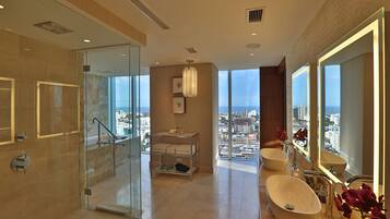 A modern bathroom with a glass shower, a vanity with a large mirror, and a view of the city.