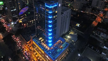 Un hôtel de grande hauteur, doté d’une façade distinctive illuminée de lumière bleue, d’une piscine sur le toit et d’un parking.