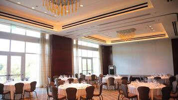 Un salón de conferencias con varias mesas dispuestas para comer, ventanas amplias y una lámpara de araña moderna.