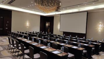 A conference room with long tables, chairs, water bottles, and a projector screen.
