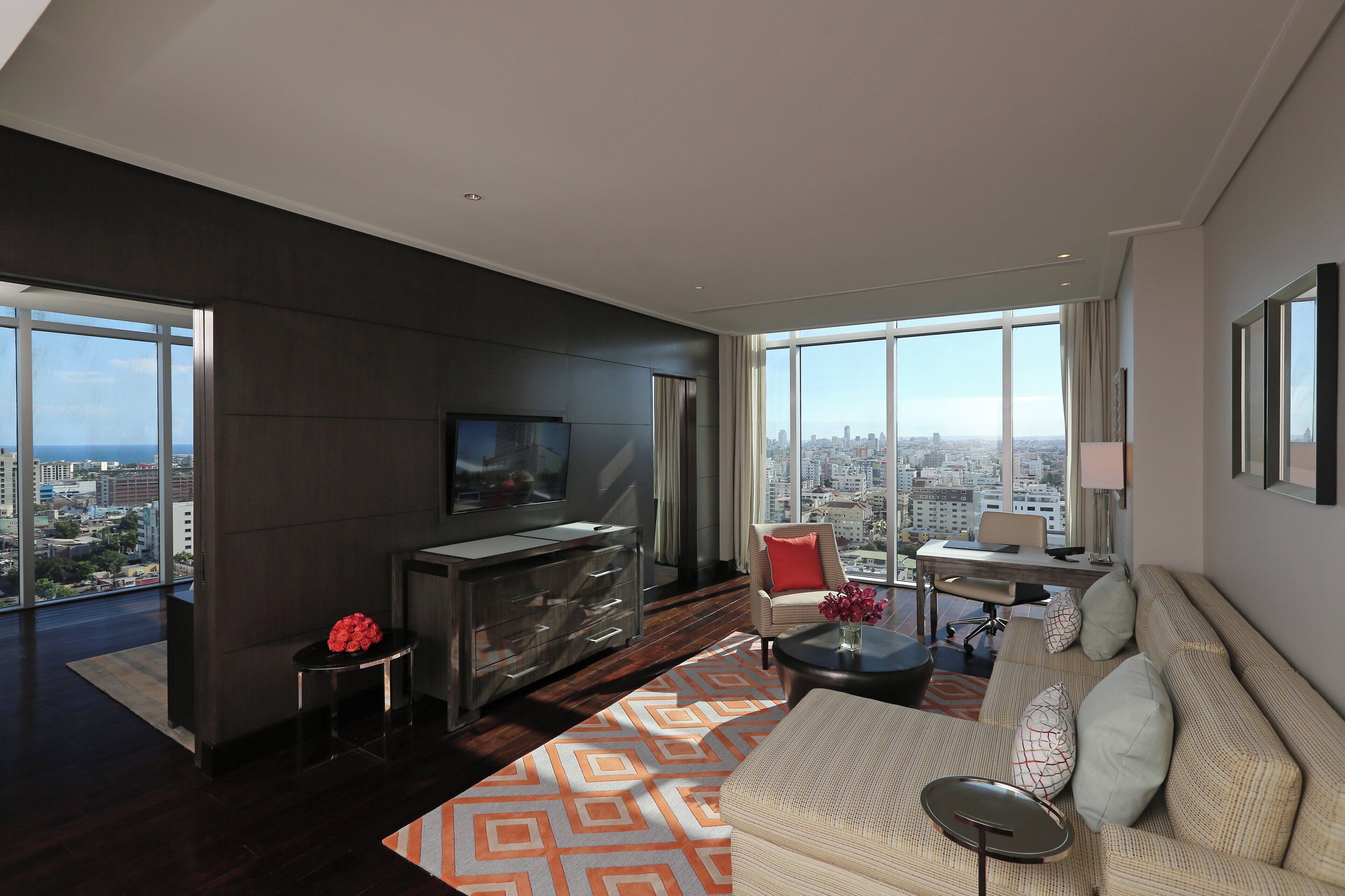 A modern living room with a large TV, a sofa, a coffee table, and a view of the city.