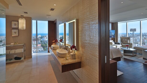 A modern bathroom with a large window, a vanity with two sinks, and a view of the city.