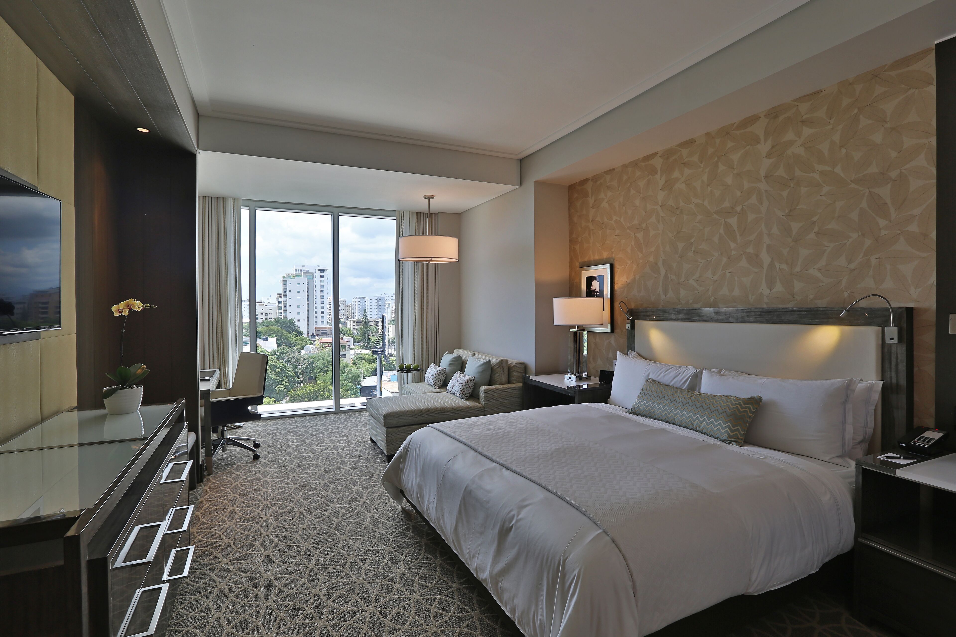 A modern hotel room with a large bed, a desk, a chair, and a TV.
