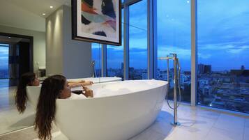 Un baño moderno con una bañera grande, ducha y vistas a la ciudad a través de amplias ventanas.