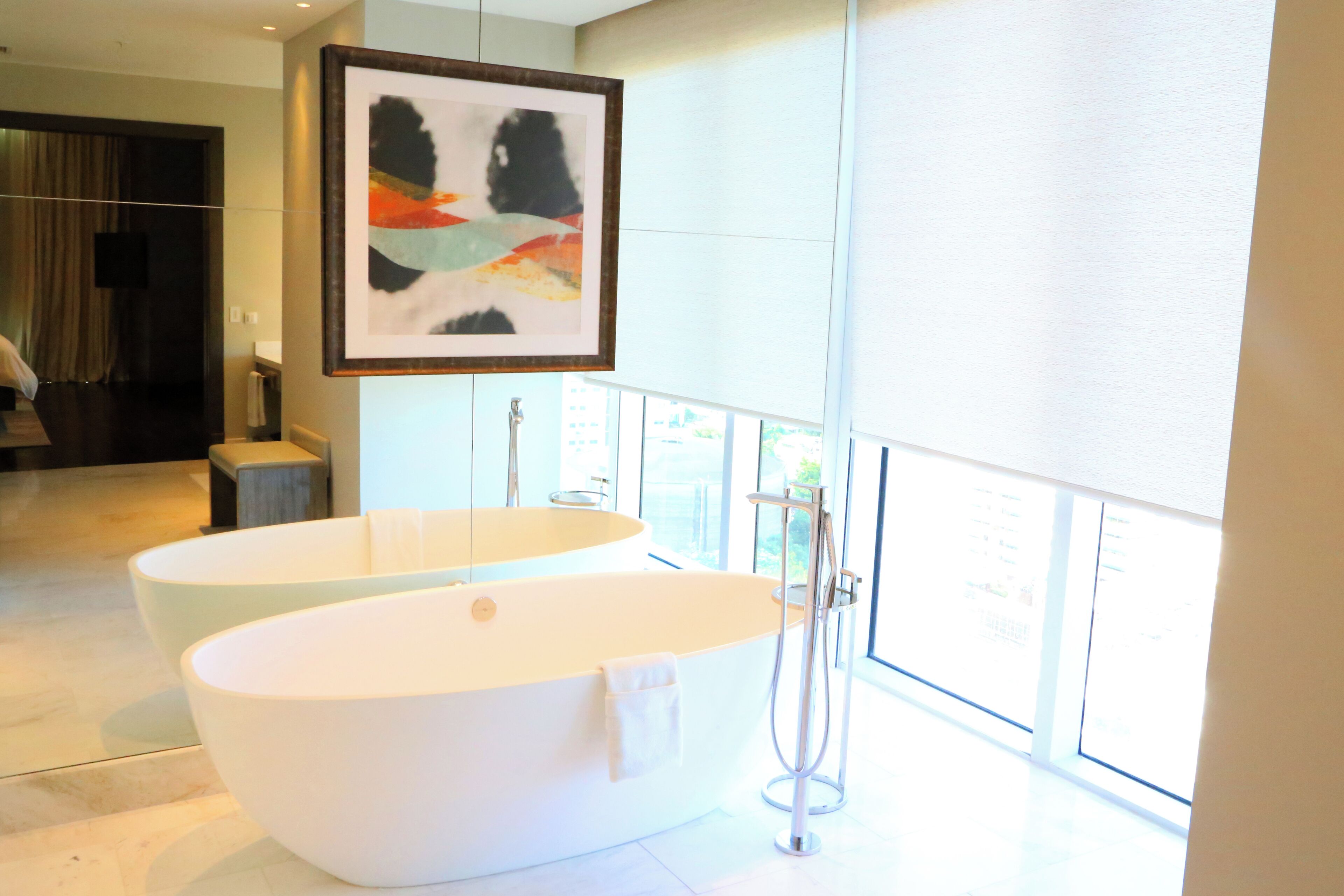 A modern bathroom with two large tubs, a framed abstract painting, and a large window providing natural light.