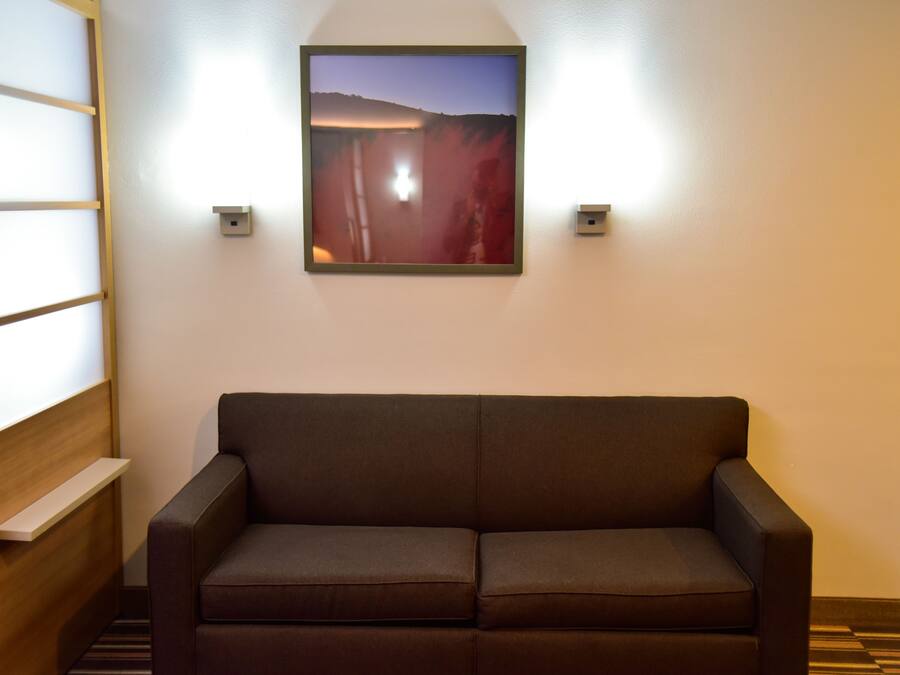 A room with a brown sofa, a framed picture on the wall, and a wooden shelf.