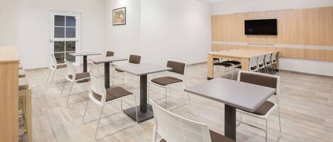 A modern conference room with multiple tables and chairs, a large flat-screen TV, and a door leading outside.