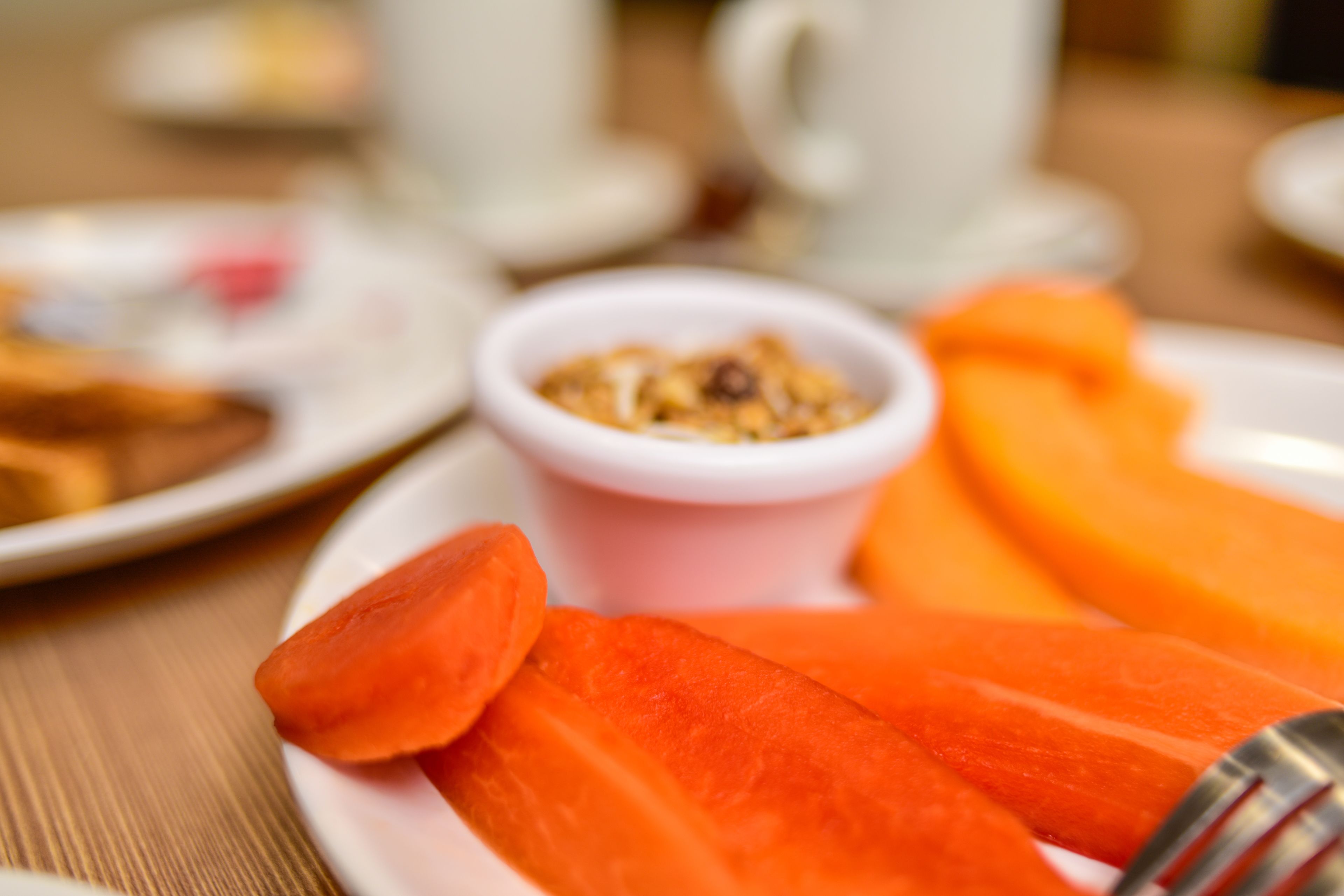 Une assiette avec des carottes coupées en tranches et un petit bol de granola.