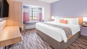 Ein Hotelzimmer mit Bett, Schreibtisch, Fernseher, Fenster mit Vorhängen und Nachttisch mit Lampe.