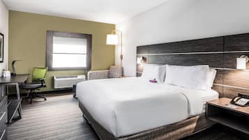 A hotel room with a large bed, a desk, a chair, a lamp, and a bedside table with a phone.