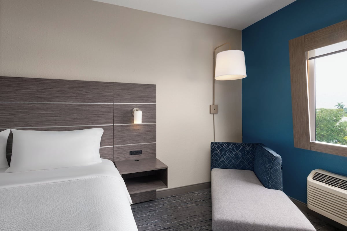 Une chambre d’hôtel comprenant un lit, une table de chevet, une lampe, un coin salon et une fenêtre donnant sur un paysage agréable.