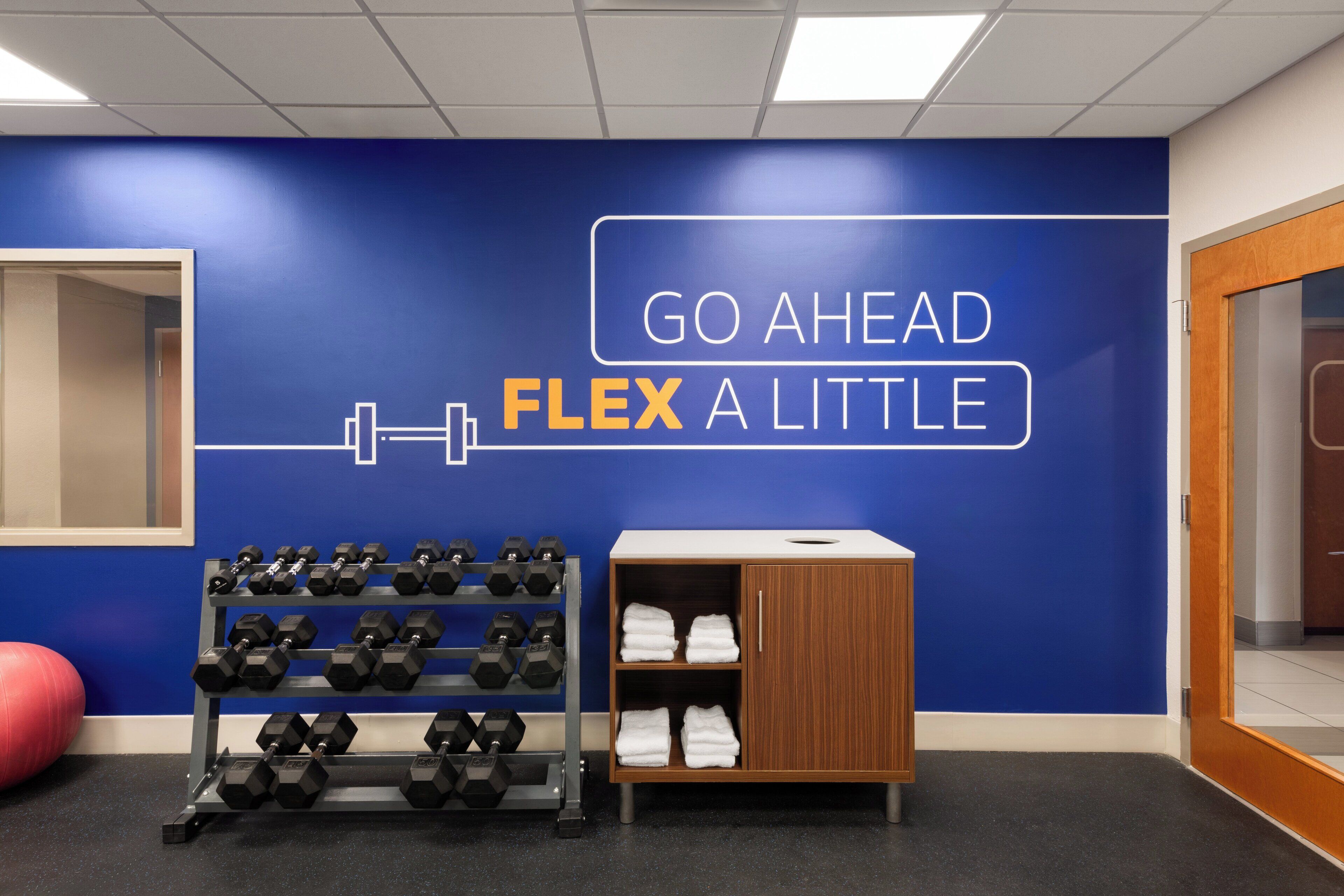 Un gimnasio con pared azul, un estante de mancuernas y un armario de madera con toallas.
