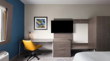 A modern hotel room with a desk, chair, television, wardrobe, and a bed.