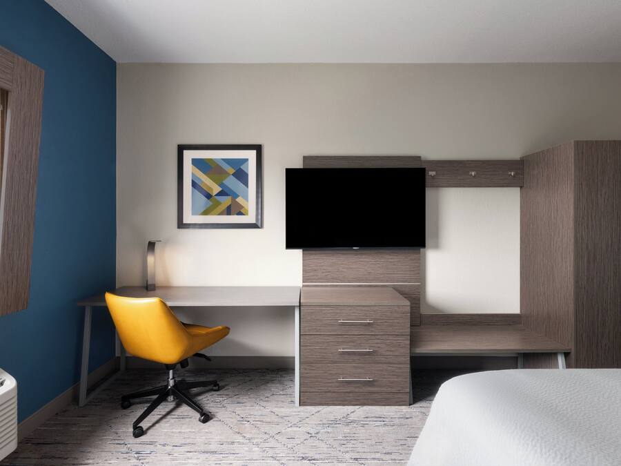 A modern hotel room with a desk, chair, television, wardrobe, and a bed.