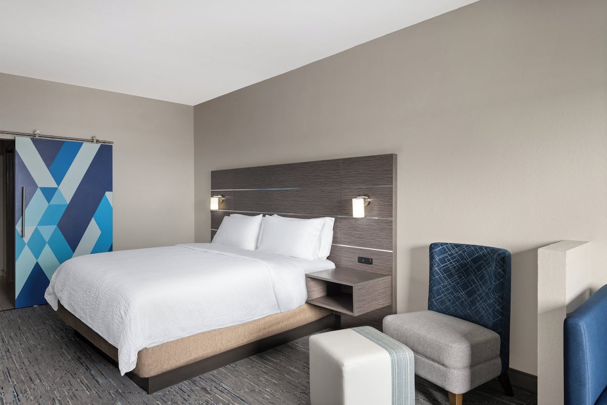 Une chambre d’hôtel moderne comprenant un lit, une table de chevet, une chaise et un rideau à motifs géométriques.
