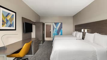 Habitación de hotel con cama, escritorio, silla, televisor y baño con ducha.