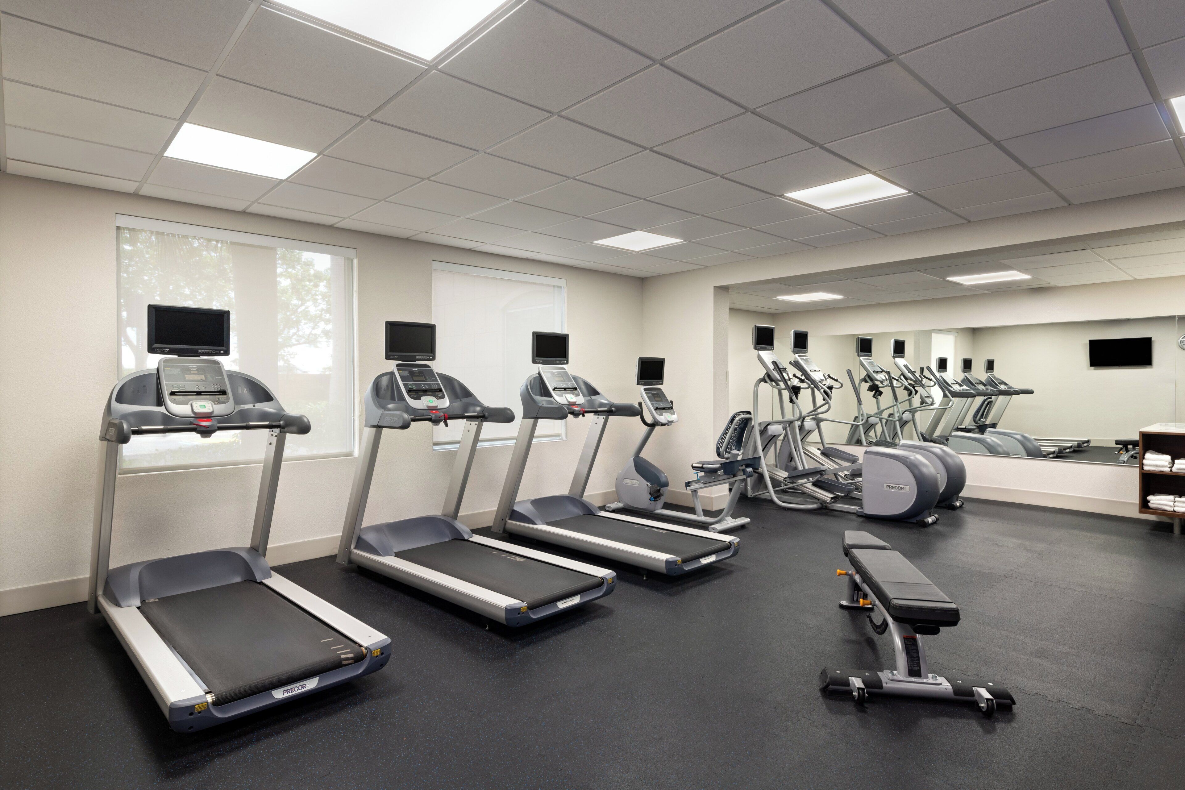 A gym with treadmills, elliptical machines, and a bench.