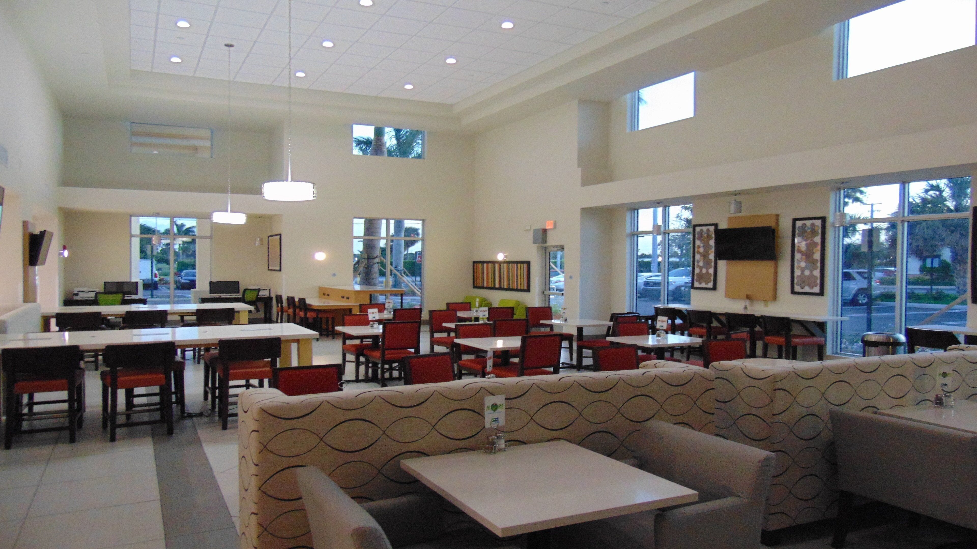A spacious indoor dining area with high ceilings, multiple tables and chairs, and large windows allowing natural light.