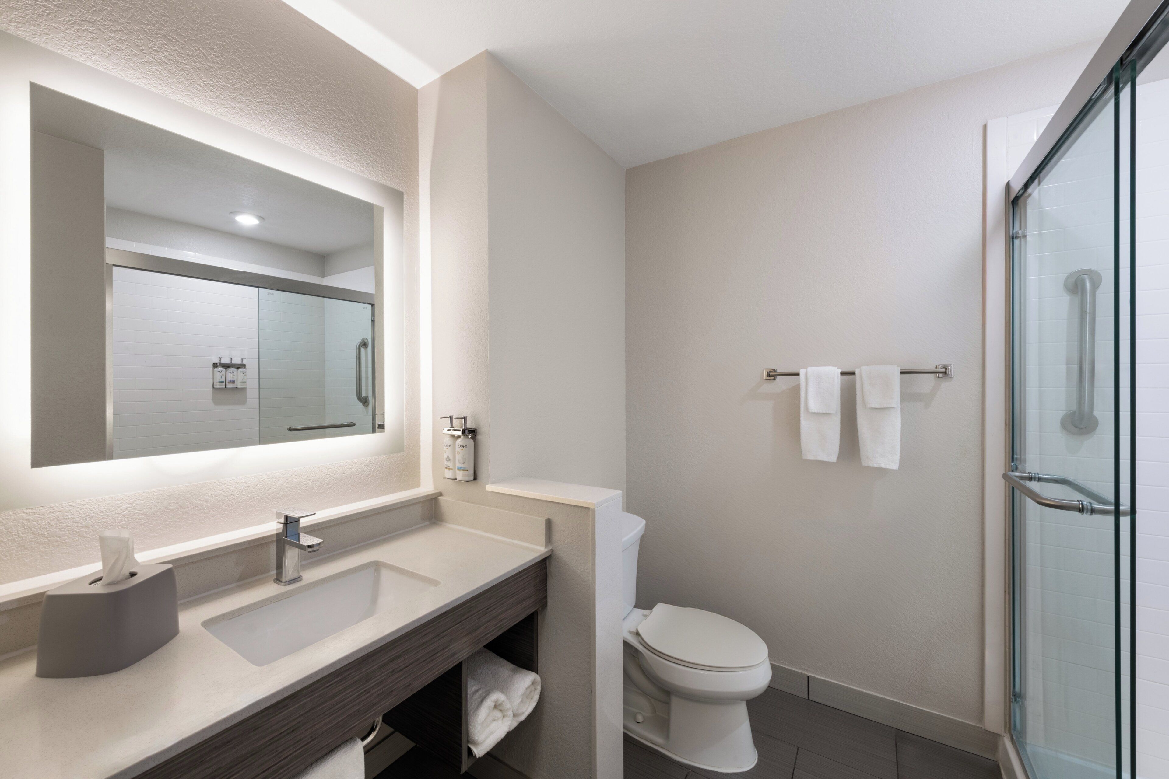 Un baño moderno con un espejo grande, un lavabo, un inodoro y una cabina de ducha de cristal.