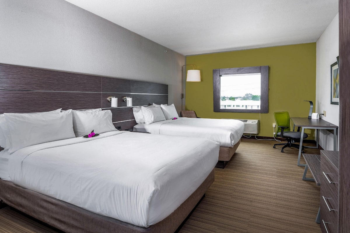 Une chambre d’hôtel avec deux lits, un bureau, une chaise et une fenêtre.