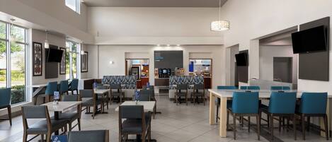 A modern dining area with multiple tables and chairs, a coffee station, and a television mounted on the wall.
