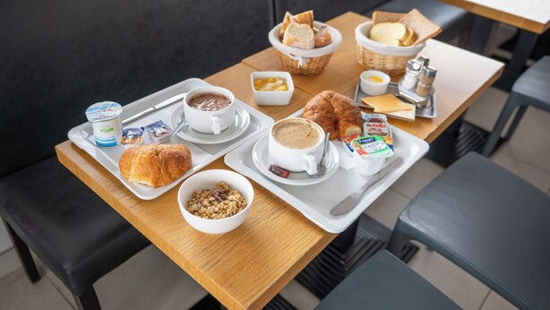 Een ontbijtplateau met croissants, koffie, yoghurt en ontbijtgranen op een houten tafel in een café.