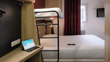 A bunk bed with a laptop on a desk, a bed with a remote control, and a window with curtains.