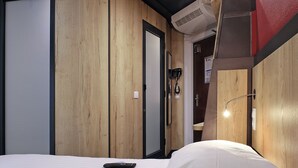 Een hotelkamer met houten wanden, een bed, een nachtkastje, een afstandsbediening en een wandairconditioner.
