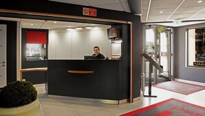 Een receptiebalie met een man erachter, een rood vluchtbord en een trap die naar een verdieping leidt.