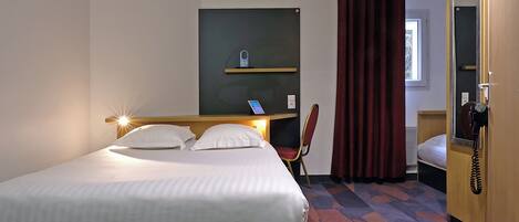 A hotel room with a bed, a desk with a phone, a chair, and a window with curtains.
