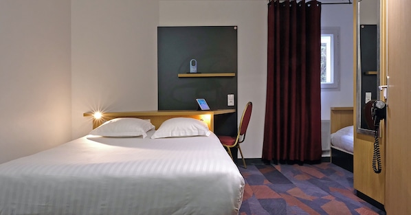 A hotel room with a bed, a desk with a phone, a chair, and a window with curtains.