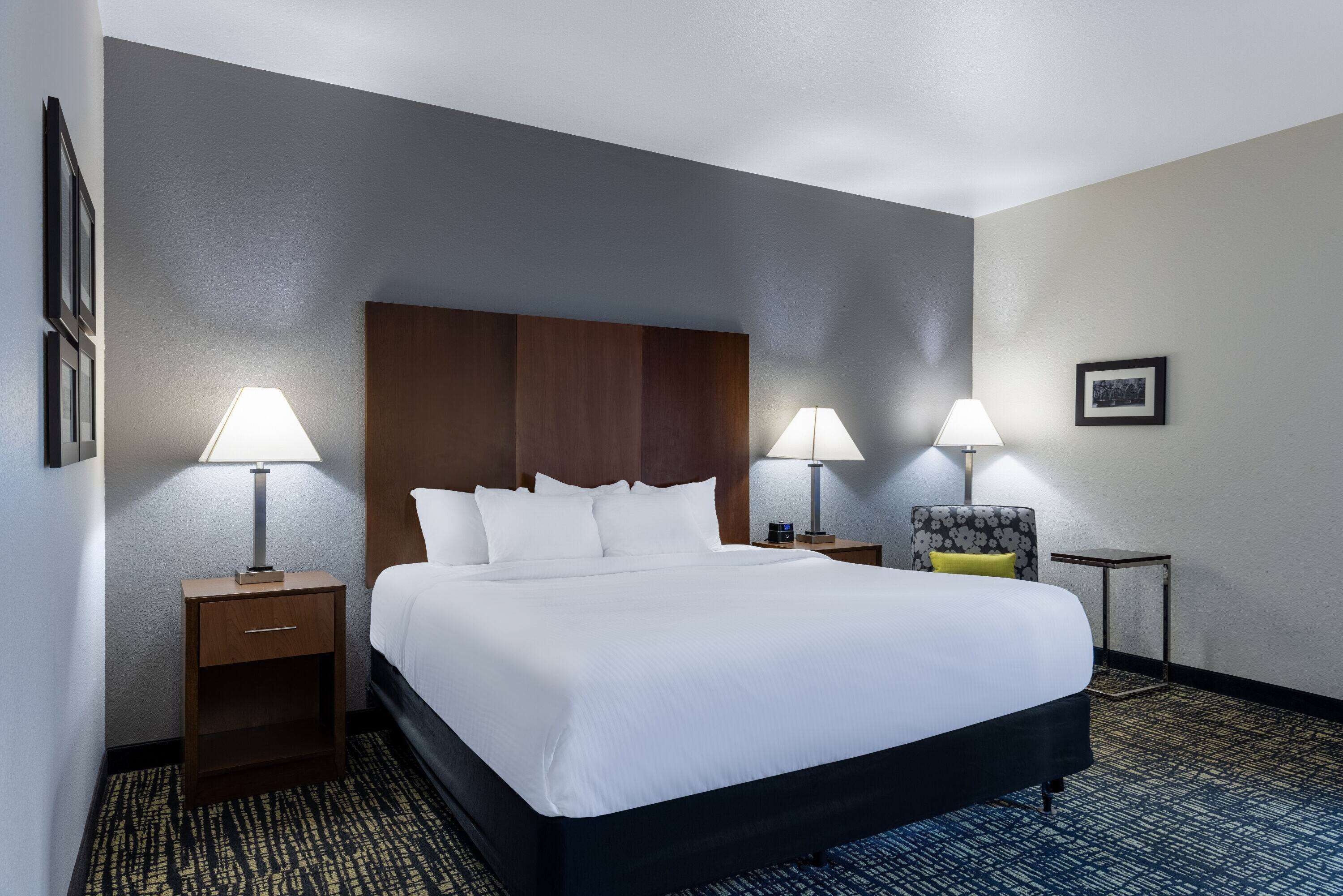 A hotel room with a large bed, two bedside tables with lamps, a small side table, and a framed picture on the wall.