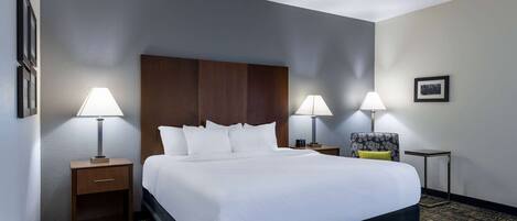 A hotel room with a large bed, two bedside tables with lamps, a small side table, and a framed picture on the wall.