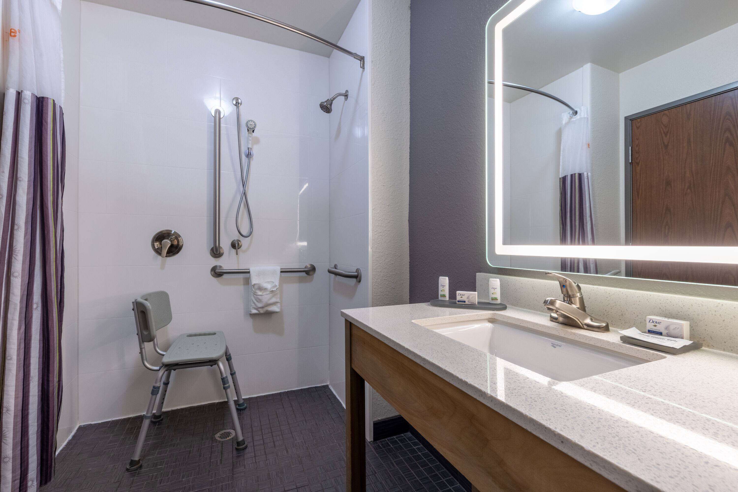 Een badkamer met een douche, een wastafel met spiegel en een stoel.